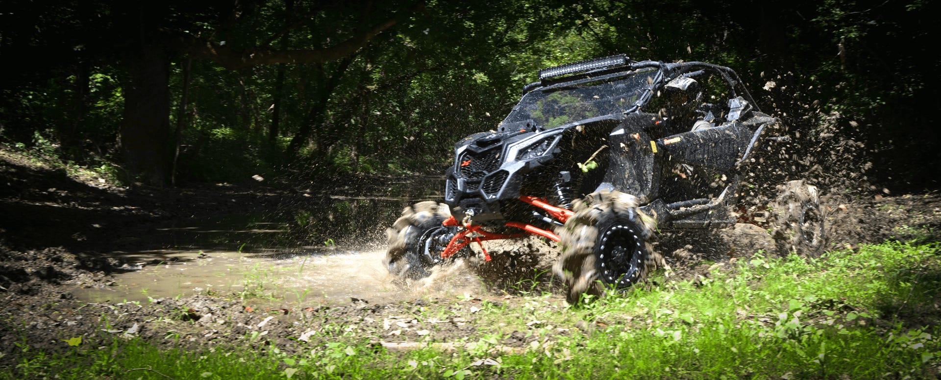 Image of a black Can-Am Maverick UTV with SuperATV half doors installed with the tires kicking up mud.