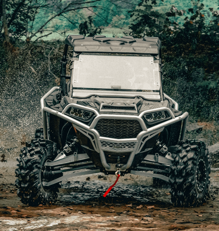 Black and silver Polaris RZR UTV tearing though the mud with a SuperATV flip windshield installed.